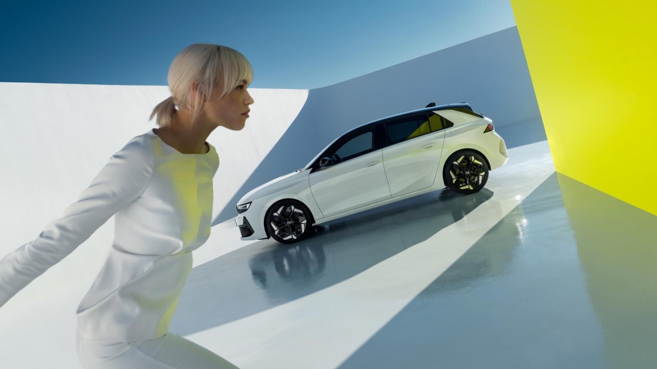 Side view of white Opel Astra GSe studio image with a woman looking on