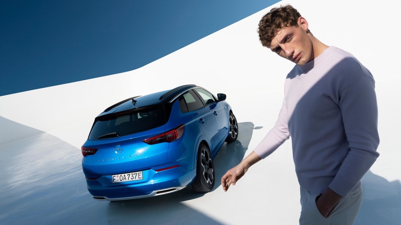Rear view of blue Opel Grandland plug-in hybrid studio image with a man standing next to the car