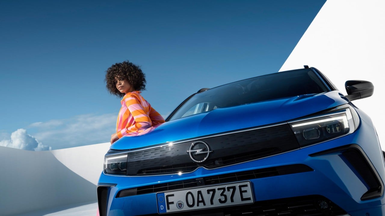 Front view of blue Opel Grandland plug-in hybrid studio image with a woman leaning against the car